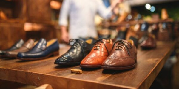 Close-up shot of elegant men's brogue shoes in a luxury leather footwear store. The shoes are displayed in a row on a wooden shelf. Defocused male customer in the background.